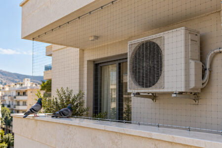 Εξωτερική μονάδα κλιματισμού σε μπαλκόνι με περιστέρια και διακριτικό δίχτυ προστασίας